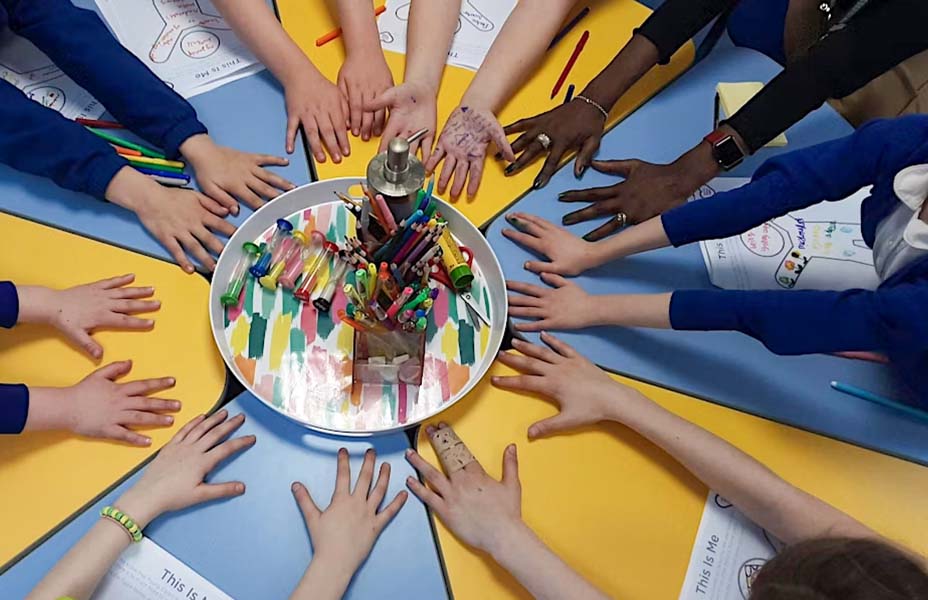 a group of young carers holding their arms out to make a circular pattern on a school table
